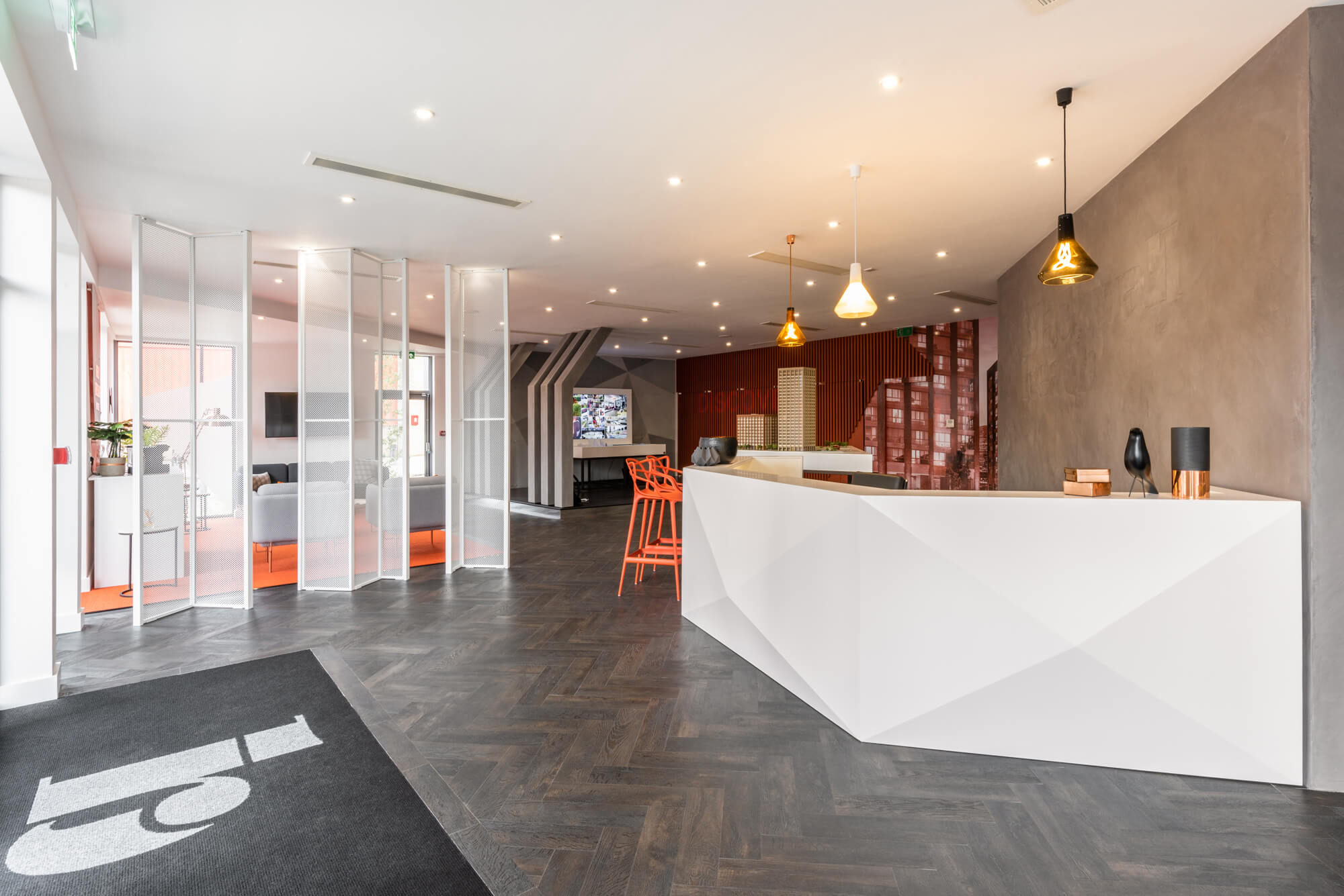 white reception desk with two orange stools placed at it and a large 3D model of a building behind it