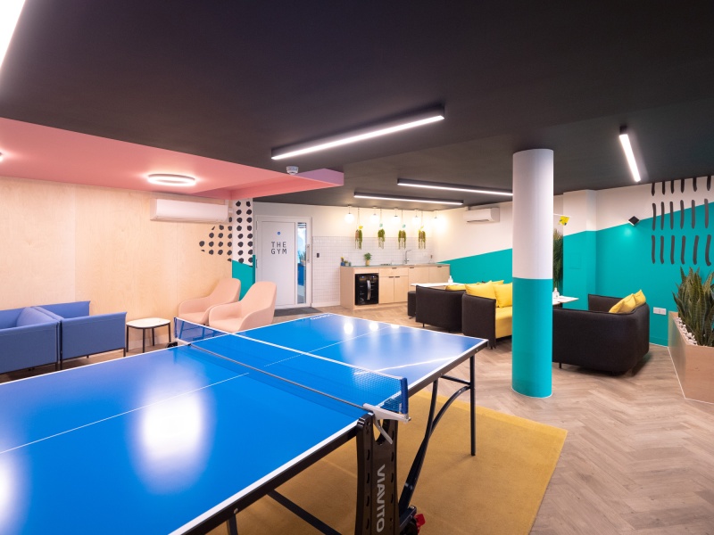 Communal area with a ping pong table in the middle of the room and seating areas dotted around the room