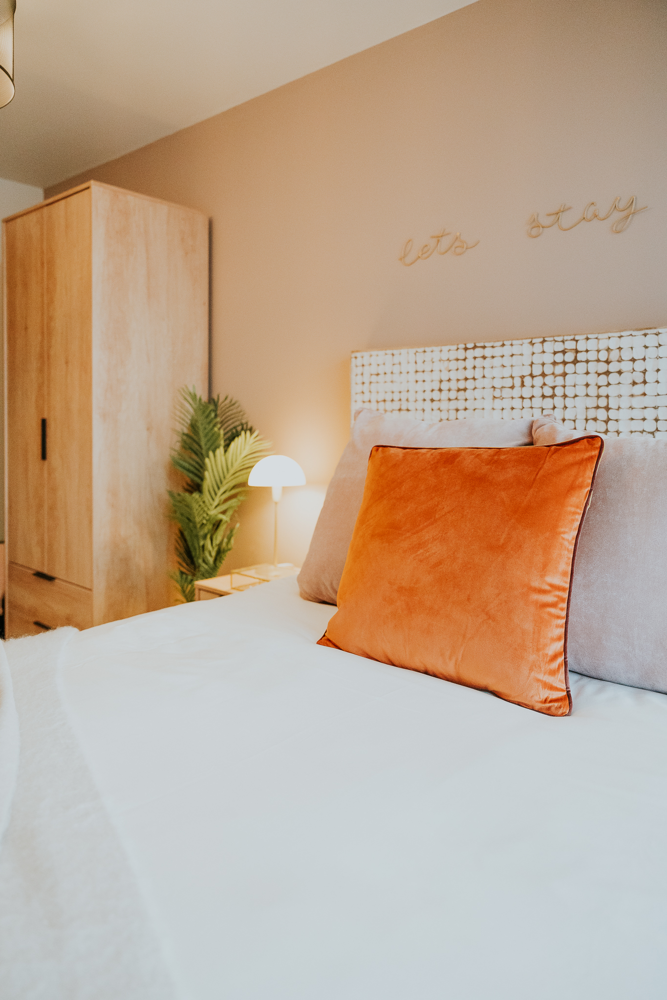 bedroom with a white bed with an orange pillow on it and a wooden wardrobe in the corner