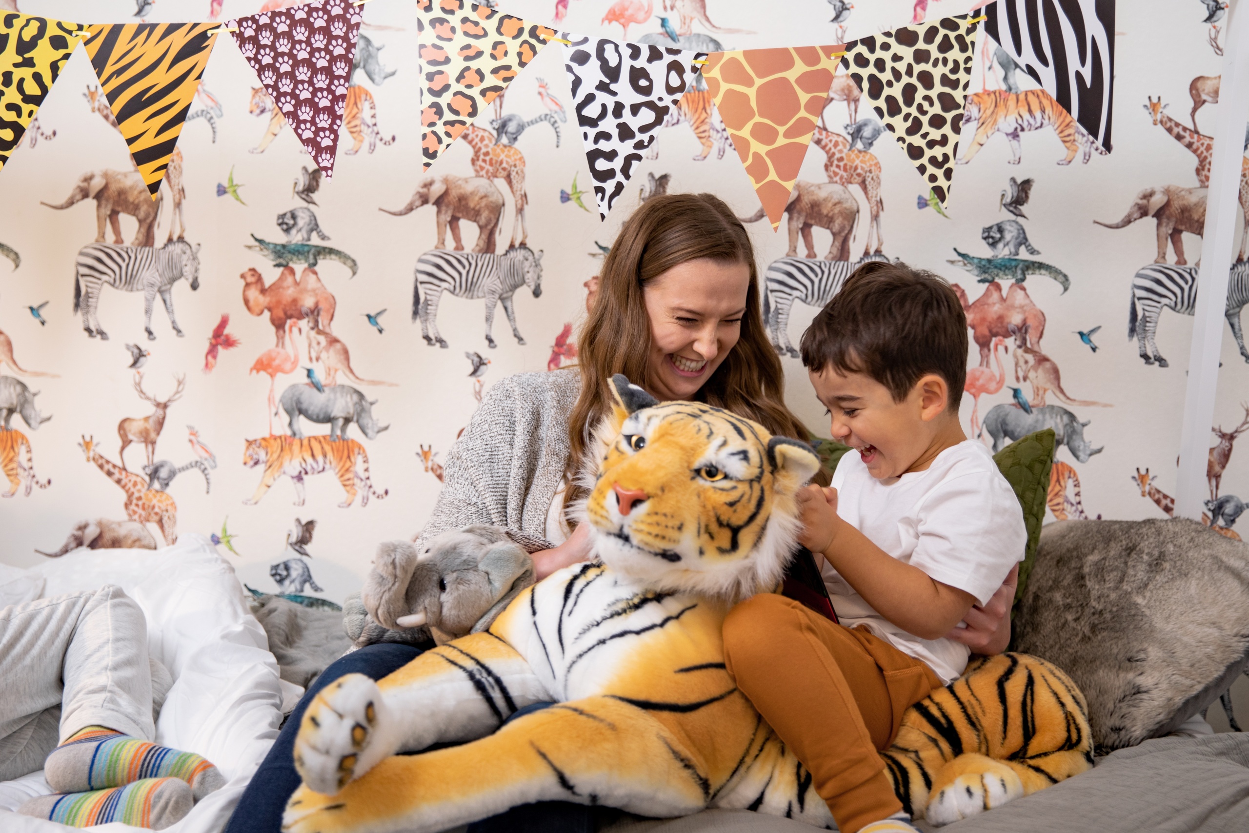 A mother and son on a bed playing with a stuffed animal tiger toy